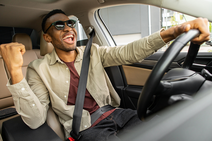 A Joyful African American In Glasses Dances In A Car, Sings Whil