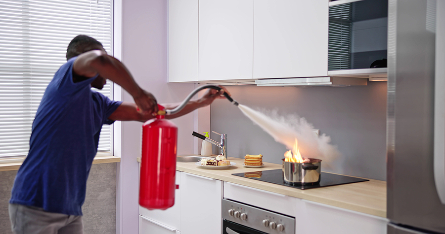 Man Using Fire Extinguisher To Stop Fire On Burning Cooking Pot