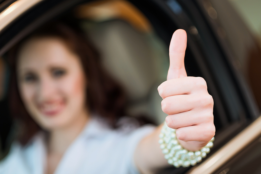 young woman in a car and showing a thumbs up